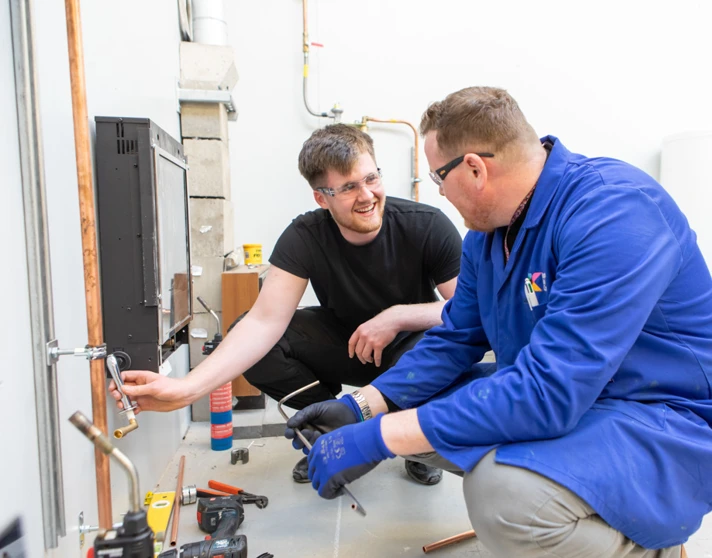 A plumbing lecturer and student smiling and collaborating closely while working together to install copper piping in a practical training session. A plumbing lecturer and student smiling and collaborating closely while working together to install copper piping in a practical training session.